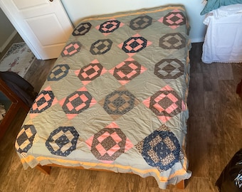 Può includere: Una trapunta vintage con un design a patchwork con quadrati rosa, blu e marroni. La trapunta è realizzata in tessuto di cotone e ha uno sfondo verde chiaro.