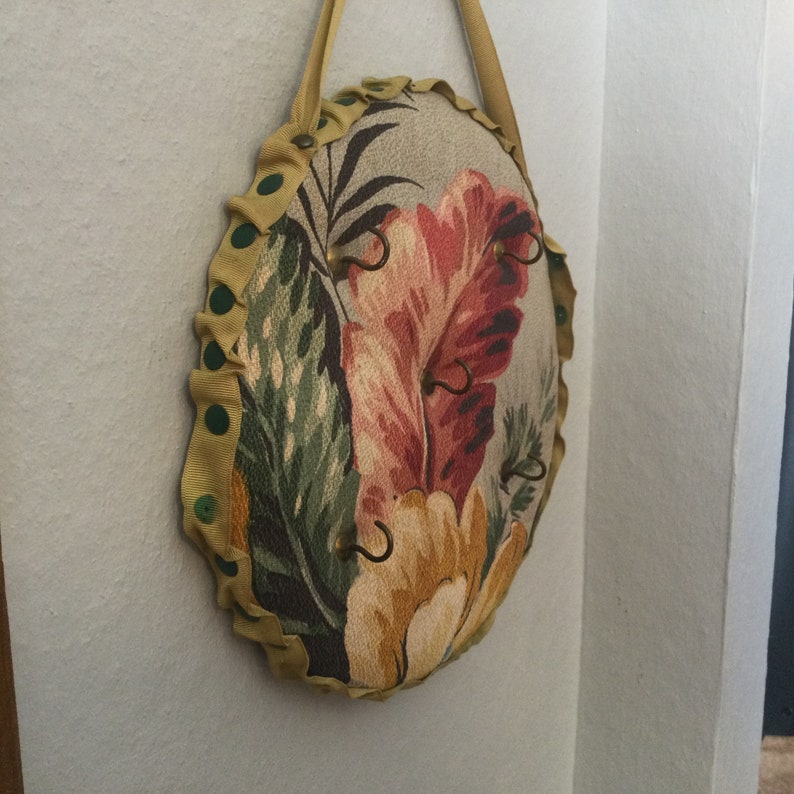 K&ouml;nnte beinhalten: Ein runder Schl&uuml;sselhalter aus Blumenstoff mit gelbem und gr&uuml;nem Besatz und vier Metallhaken.