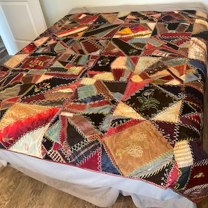 May include: A large patchwork quilt featuring a complex arrangement of multi-colored fabric scraps in various shapes and textures. The pieces are joined by visible decorative embroidery stitching, with some patches displaying embroidered floral motifs.