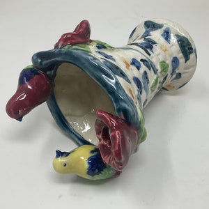 Op de afbeelding: Een keramische vaas met een blauw, wit en groen bloemenpatroon. De vaas is gevormd als een hoed en heeft drie kleine vogels die eraan vastzitten. De vogels zijn geschilderd in tinten rood, geel en blauw.