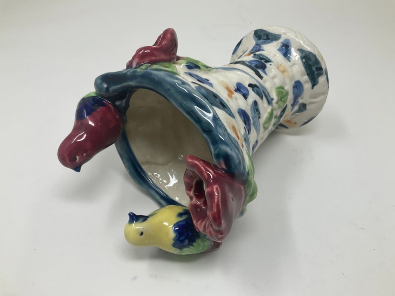 Op de afbeelding: Een keramische vaas met een blauw, wit en groen bloemenpatroon. De vaas is gevormd als een hoed en heeft drie kleine vogels die eraan vastzitten. De vogels zijn geschilderd in tinten rood, geel en blauw.