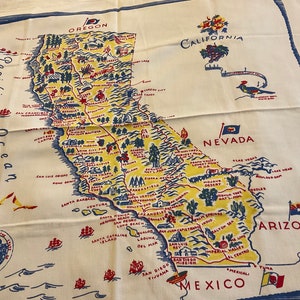 May include: A vintage map of California, Oregon, Nevada, and Arizona printed on a white fabric tablecloth. The map is in a colorful cartoon style with blue, red, and yellow accents. The map includes major cities and landmarks. The text "Pacific Ocean" is printed on the left side of the map.