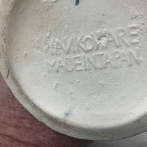 Op de afbeelding: Close-up van de onderkant van een witte keramische vaas met de tekst "Hawkoare Made in Japan" in zwart gestempeld.