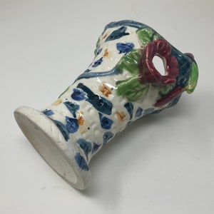 Op de afbeelding: Een witte keramische vaas met een blauw, groen en rood bloemenontwerp. De vaas heeft een brede opening en een smalle basis.