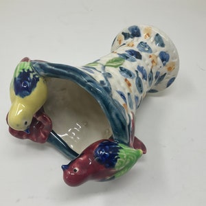 Op de afbeelding: Een keramische vaas met een blauw en wit bloemenpatroon en twee vogels die op de rand zitten. De vaas is gevormd als een mand en heeft een brede opening.