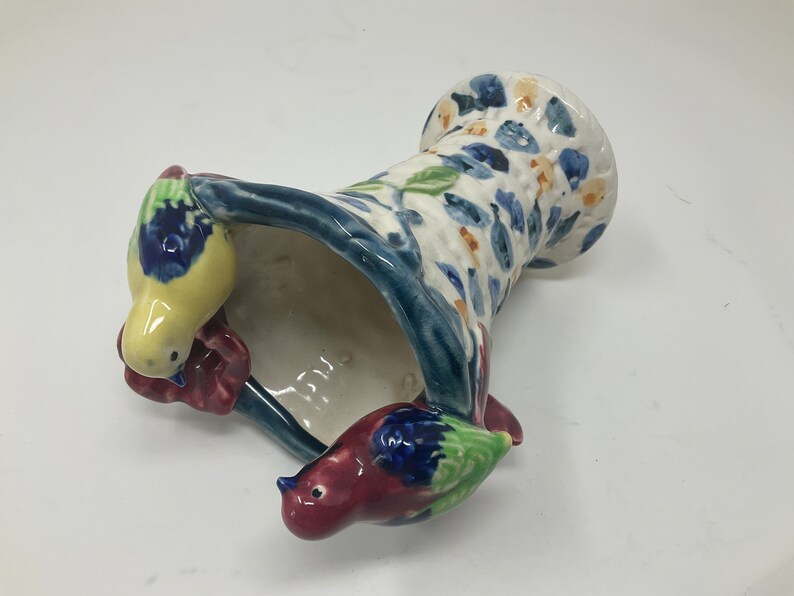 Op de afbeelding: Een keramische vaas met een blauw en wit bloemenpatroon en twee vogels die op de rand zitten. De vaas is gevormd als een mand en heeft een brede opening.
