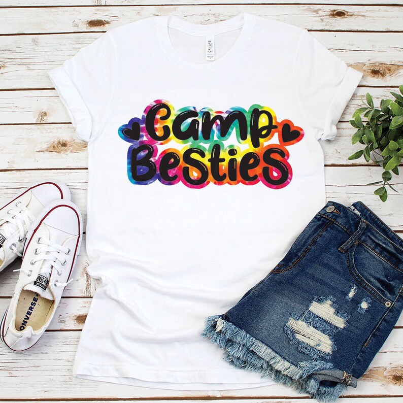 May include: White t-shirt with a tie-dye design and the text "Camp Besties" in black lettering.