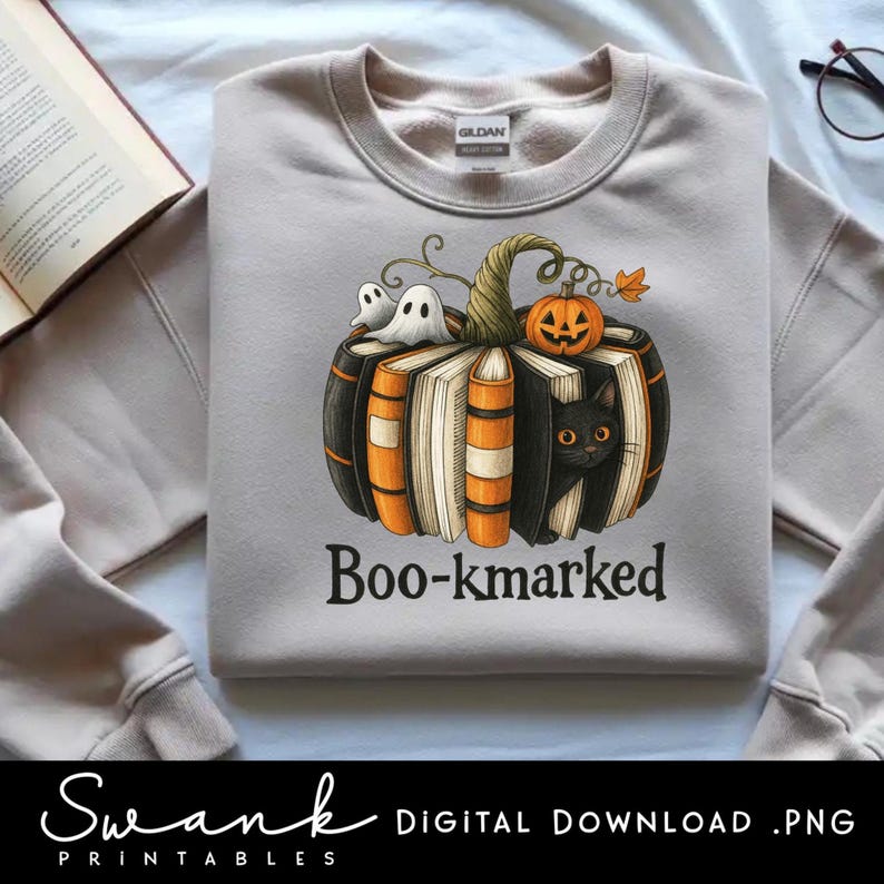 K&ouml;nnte beinhalten: Hellgraues Sweatshirt mit einem Halloween-Motiv. Die Grafik zeigt einen K&uuml;rbis aus B&uuml;chern, mit einer schwarzen Katze, Geistern und einer Jack-o'-Lantern. Der Text "Boo-kmarked" ist darunter gedruckt.