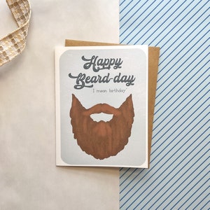 May include: A greeting card with a gray background and a brown beard illustration. The text on the card reads "Happy Beard-day I mean birthday."