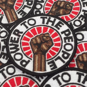 May include: Close-up of several black and white embroidered patches with a raised fist and the text "Power to the People".