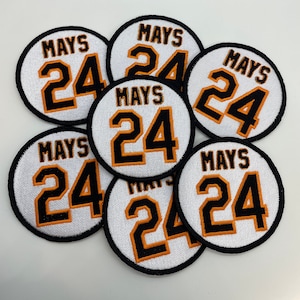 May include: Seven white, round, embroidered patches with black outlines. Each patch features the name "MAYS" and the number "24" in orange and black.