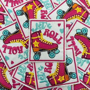 Puede incluir: Parches bordados cuadrados blancos con un diseño de patín rosa, estrellas y cordones amarillos, y ruedas turquesas. El texto "Let's Roll" está en turquesa y rosa.