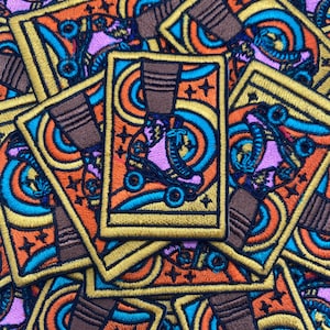 May include: Embroidered patches featuring a roller skate design. The patches have a rectangular shape with a gold border. The roller skate is depicted in a vibrant color palette of orange, blue, pink, and brown. The patches are scattered.