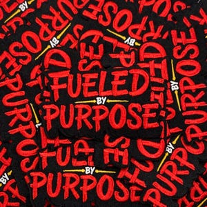 May include: Black embroidered patches with the words "Fueled By Purpose" in red. The patches have a black background with red text and yellow accents. The patches are a motivational item.