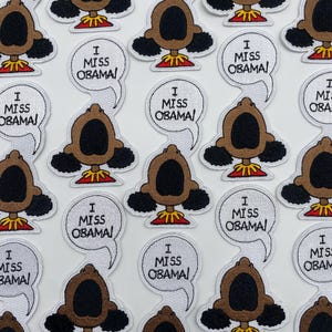 May include: A collection of embroidered patches featuring a cartoon character with the text "I Miss Obama!" in a speech bubble. The patches are white with black outlines and feature a brown character with black hair and a red shirt.