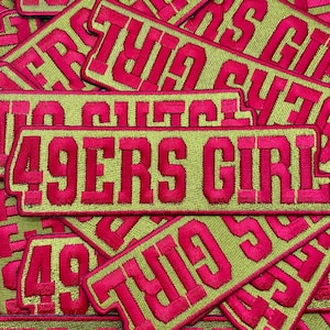 May include: A close-up of several embroidered patches with the words "49ers Girl" in pink lettering on a green background.