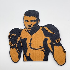 Puede incluir: Parche bordado que representa a un boxeador en negro y beige. El parche presenta un retrato del boxeador con guantes de boxeo negros y una expresión decidida. El parche está diseñado para aplicarse en ropa o accesorios.