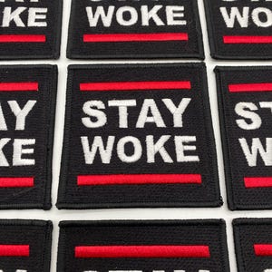 May include: Nine black fabric patches with red and white embroidery. Each patch reads "STAY WOKE" in white letters with two red lines above and below the text.