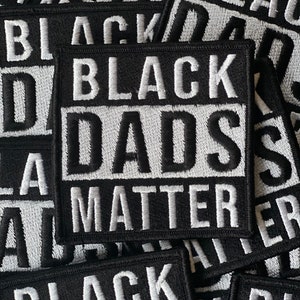 Op de afbeelding: Close-up van verschillende zwarte stoffen patches met witte geborduurde tekst die "Black Dads Matter" luidt.