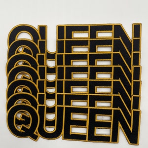 May include: A stack of ten black and gold iron-on patches that spell out the word "QUEEN".