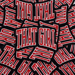 Könnte beinhalten: Eine Ansammlung schwarzer, gestickter Aufnäher mit dem Text "THAT GIRL" in einer kräftigen Schriftart im College-Stil. Die Schrift ist rot mit weißer Umrandung, und die Aufnäher haben einen schwarzen Rand.