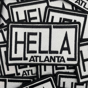 May include: A stack of white and black embroidered patches with the word "HELLA" and the text "ATLANTA" in black lettering.