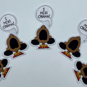 May include: Six iron-on patches featuring a cartoon character with the text "I Miss Obama!" in a speech bubble. The character is brown with a large mouth and black hair.