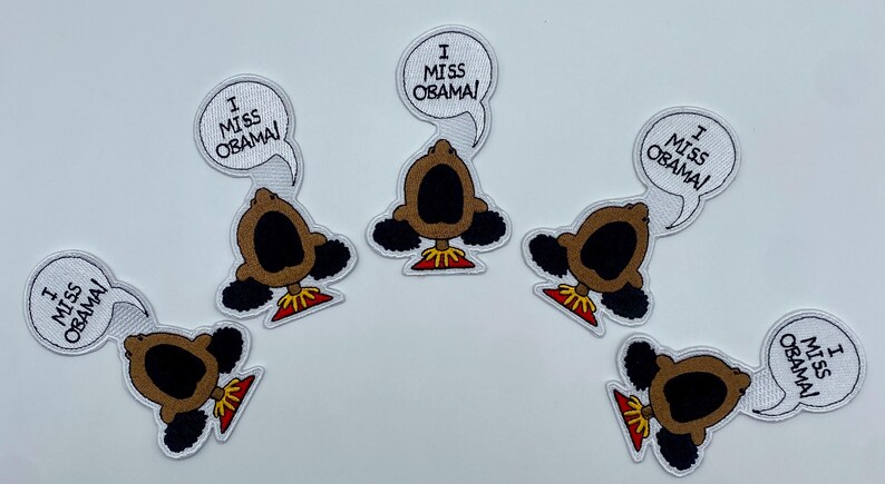 May include: Six iron-on patches featuring a cartoon character with the text "I Miss Obama!" in a speech bubble. The character is brown with a large mouth and black hair.