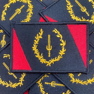 May include: A stack of black and red fabric patches with a gold embroidered design of a sword and wreath. The patches are sewn with a black thread.