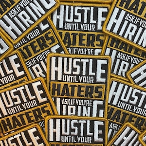 May include: A close-up of several black and gold embroidered patches with the text "Hustle Until Your Haters Ask If You're Hiring".