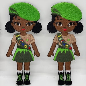 May include: Two embroidered patches of a girl scout in a green beret, brown shirt, green skirt, and black boots. The girl scout is wearing a sash with colorful badges.