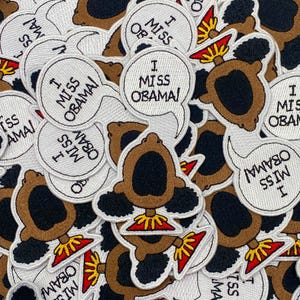 May include: A collection of white embroidered iron-on patches featuring a cartoon character with an afro and the text "I Miss Obama!"