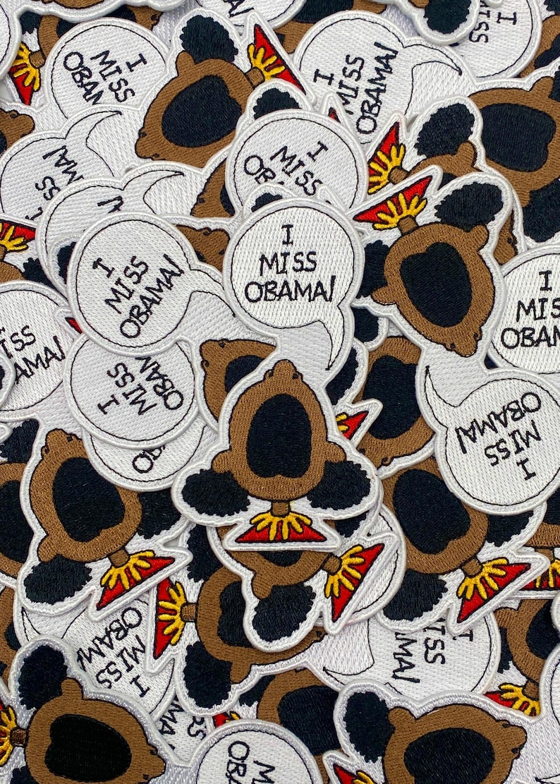May include: A collection of white embroidered iron-on patches featuring a cartoon character with an afro and the text "I Miss Obama!"