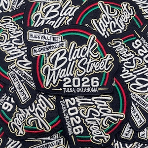 May include: A black embroidered patch featuring the text Black Wall Street and 2026, with street signs reading Black Wall Street and N. Greenwood Ave, accented by red and green circular lines and the text Tulsa, Oklahoma in white thread.
