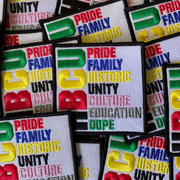Op de afbeelding: Een stapel kleurrijke geborduurde patches met de woorden "Pride Family Historic Unity Culture Education Dope" erop. De patches zijn gemaakt van witte stof met zwarte randen en hebben een regenboog aan kleuren.