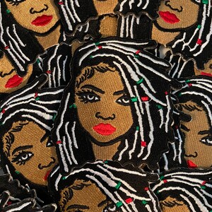 May include: Embroidered patches featuring a woman's face with black and white dreadlocks, red lips, and a gold skin tone. The patches have a black border and are scattered across the image.