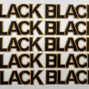 May include: Multiple black patches with the word "BLACK" in a bold, blocky font. Each letter is outlined in gold, creating a striking contrast against the black. The patches are arranged in rows on a white background.