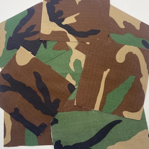 May include: Several fabric swatches with a camouflage pattern. The pattern features a mix of brown, black, tan, and green colors. The fabric has a ribbed texture.