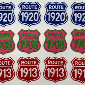 Könnte beinhalten: Zwölf schildförmige gestickte Aufnäher in drei Reihen angeordnet. Die oberste Reihe zeigt vier blaue Aufnäher mit weißem Text ROUTE 1920. Die mittlere Reihe hat vier pinke Aufnäher mit grünem Text ROUTE 1908. Die untere Reihe enthält vier rote Aufnäher mit weißem Text ROUTE 1913.