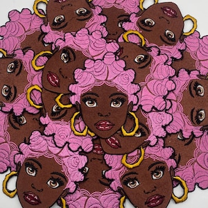 May include: A collection of embroidered patches featuring a Black woman with brown skin, pink hair, and gold hoop earrings. The patches have a brown background and are intricately detailed with a cartoon-like design.