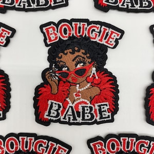 May include: An embroidered patch featuring a character with dark skin and black hair, wearing red cat-eye sunglasses, a red feather boa, and cherry earrings. The text BOUGIE is embroidered in red above the character and BABE in white below.