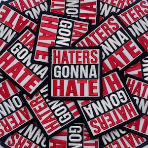 May include: A collection of square embroidered patches featuring the text HATERS GONNA HATE in bold red and white lettering. Each patch has a black border and is arranged in a repeating pattern, showcasing the embroidered fabric texture.