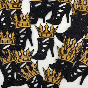 May include: Black high-heeled shoe patches with gold embroidered crowns. The patches feature a cutout design and are arranged in a scattered pattern. The crowns are detailed with gold thread, adding a touch of elegance to the design. These patches are suitable for various craft projects.