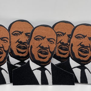 May include: Five embroidered patches featuring a portrait of Martin Luther King Jr. in a suit and tie. The patches are brown and black with a white background.
