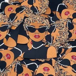 May include: A collection of fabric patches featuring a stylized illustration of a person with curly blonde hair, wearing black cat-eye sunglasses with white rhinestone accents, red lipstick, and a white beaded necklace against a solid black background.