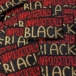 May include: A close-up of several black fabric patches with gold and red embroidery. The patches read "Unapologetically Black".