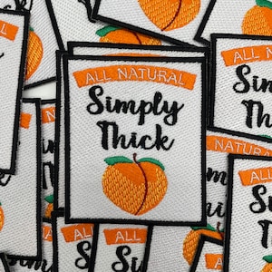 May include: A stack of white fabric patches with black stitching. The patches feature a peach design and the text "All Natural Simply Thick".