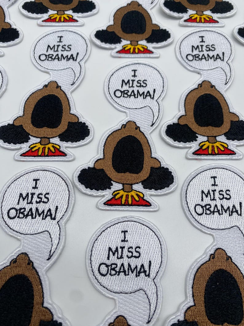 May include: A collection of embroidered patches featuring a cartoon character with a speech bubble that says "I Miss Obama". The character has brown skin, black hair, and a red shirt.
