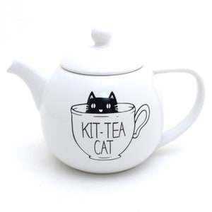May include: White ceramic teapot with a black cat illustration inside a teacup. The text "Kit-Tea Cat" is printed on the teapot.