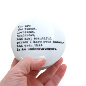 May include: White ceramic trinket box with a black typewriter font inscription that reads: "You are the finest, loveliest, tenderest, and most beautiful person I have ever known- and even that is an understatement."